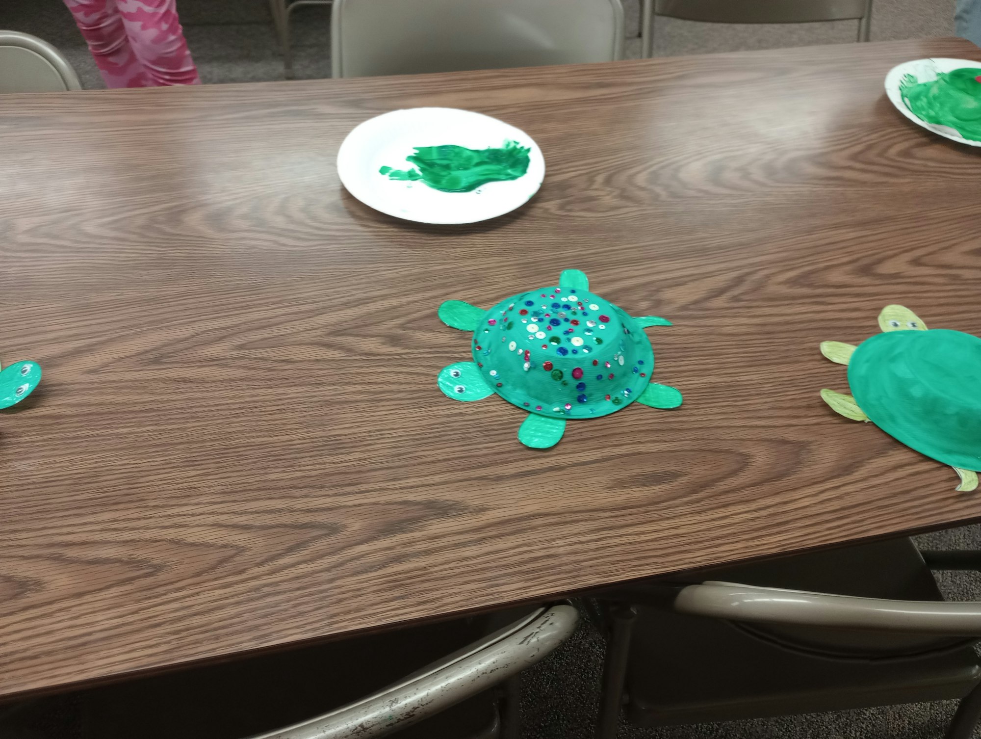Paper plate turtle crafts with green paint and sequins on a table.