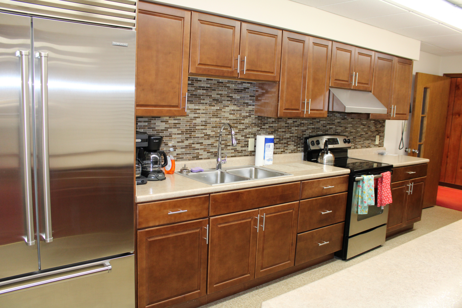 A modern kitchen featuring stainless steel appliances, brown cabinets, a tiled backsplash, and a tidy countertop.