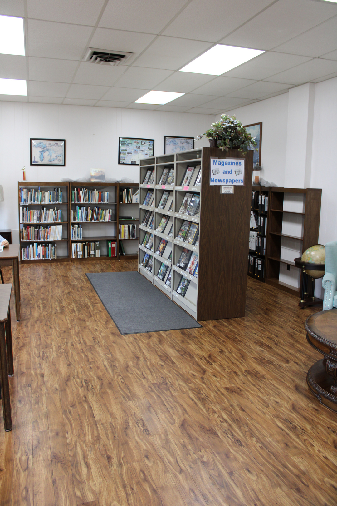 The image shows a cozy library interior featuring bookshelves, magazines, a globe, and wooden flooring.