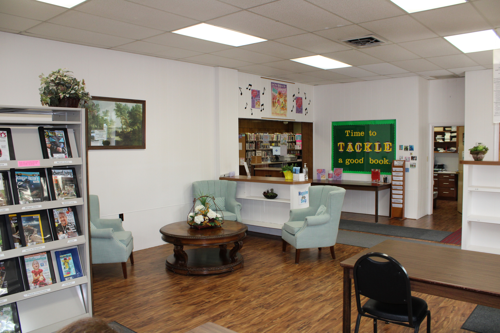A cozy library space with seating, a coffee table, a book display, and a sign encouraging visitors to enjoy reading.