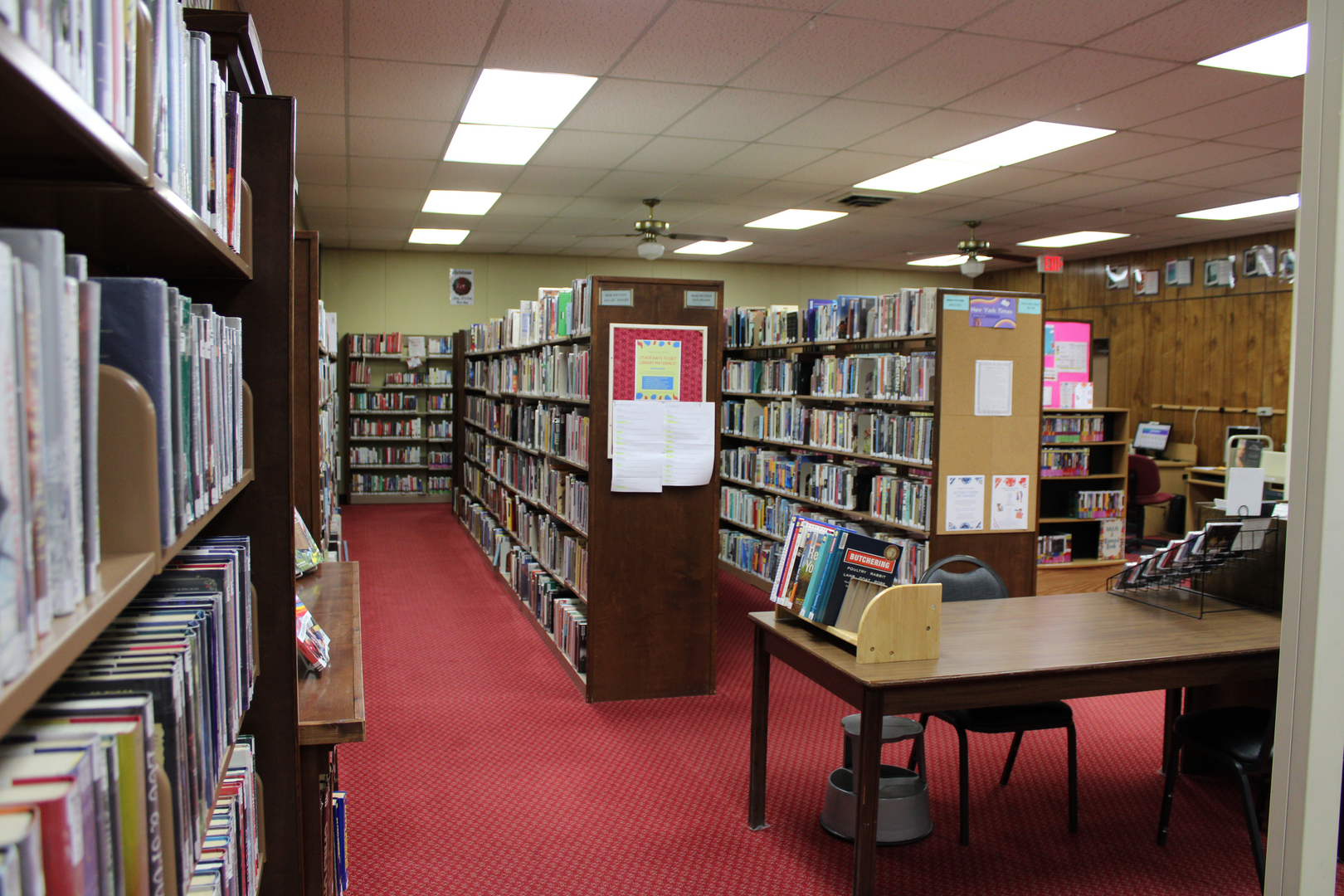 A cozy library with bookshelves lining the walls, a red carpet, and a small study area with a table and chairs.