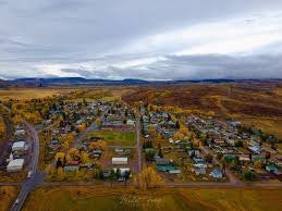 Aerial view of a small town surrounded by grassy fields and hills, with a mix of residential and commercial buildings.