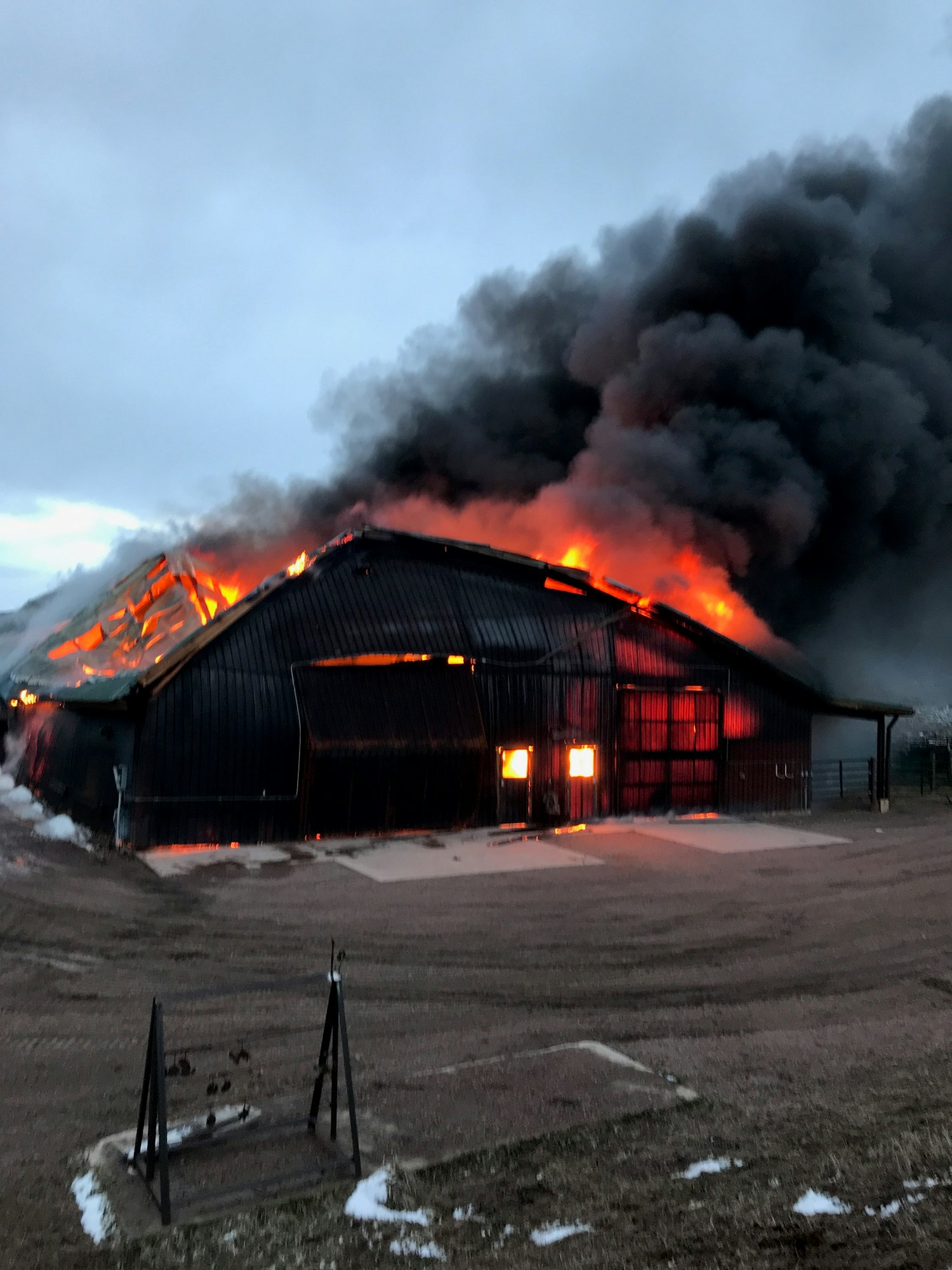 A barn is engulfed in flames, emitting thick black smoke against a cloudy sky.