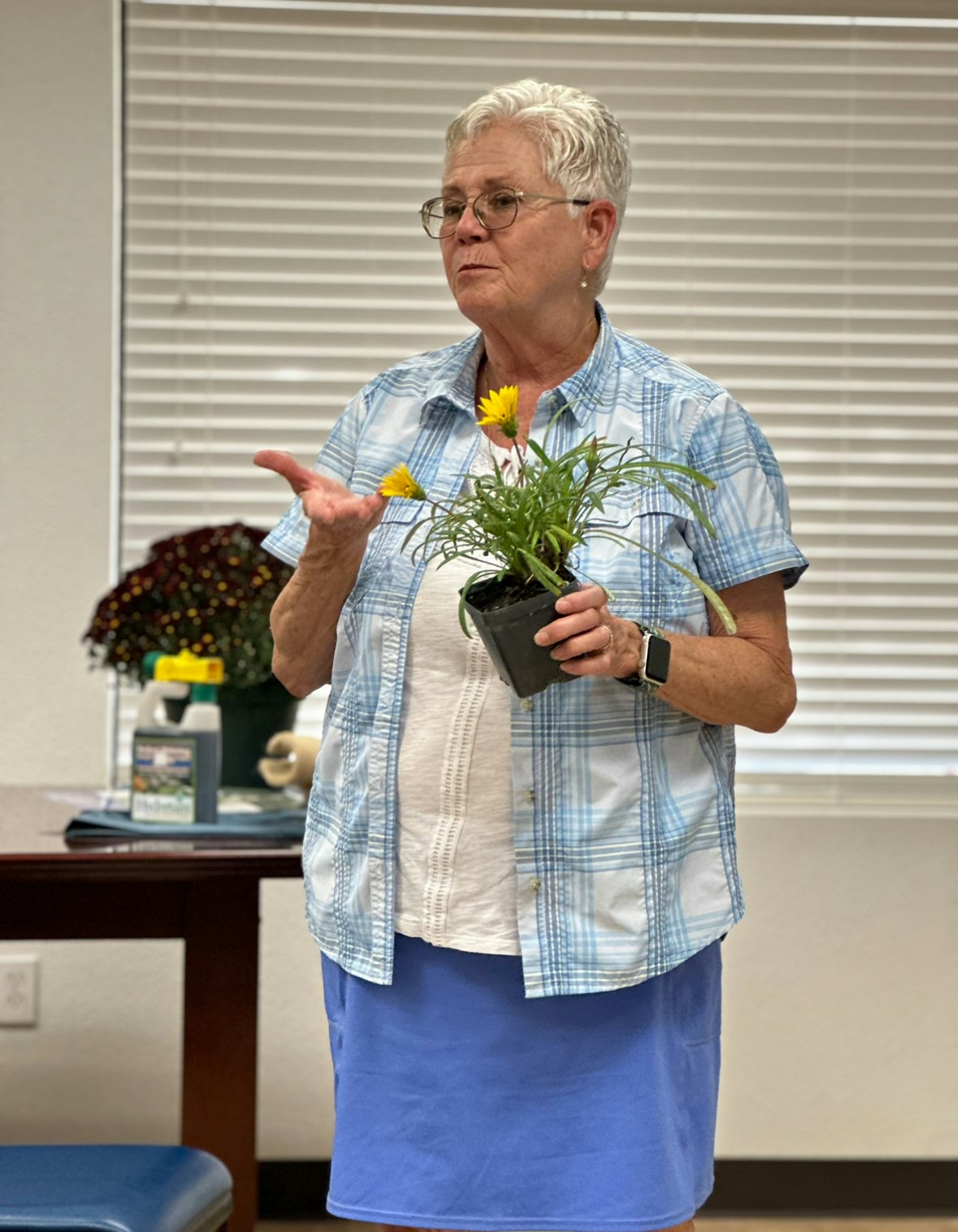 Terri Johansen of Johansen Nursery & Landscaping presenting a potted flower indoors, engaging with an audience not visible in the photo.