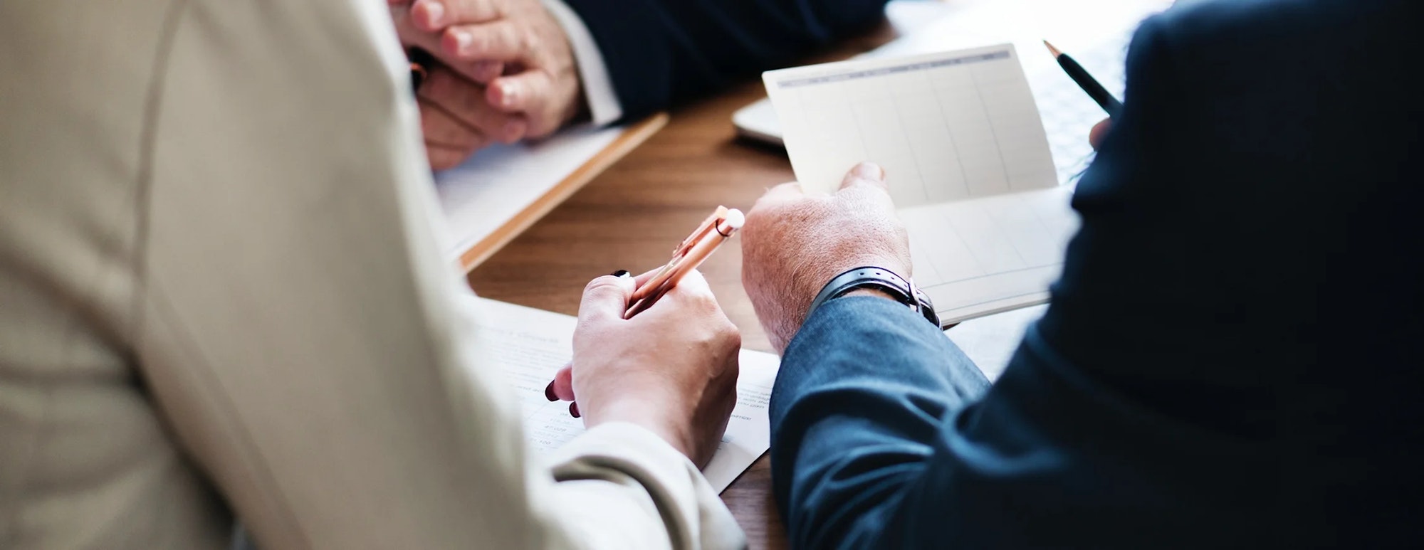 People in a meeting with documents and a pen, likely discussing business.