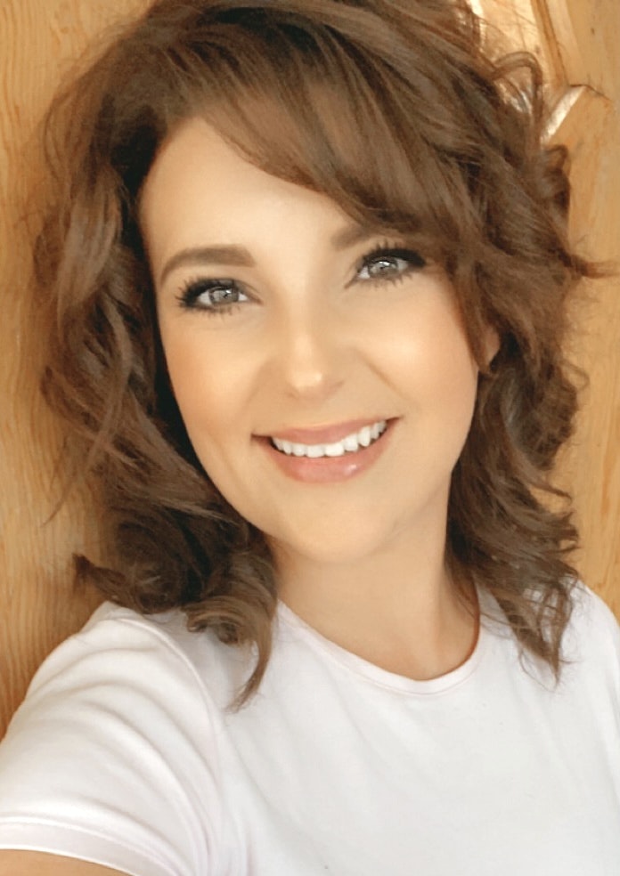 A smiling person with curly hair against a wooden background.
