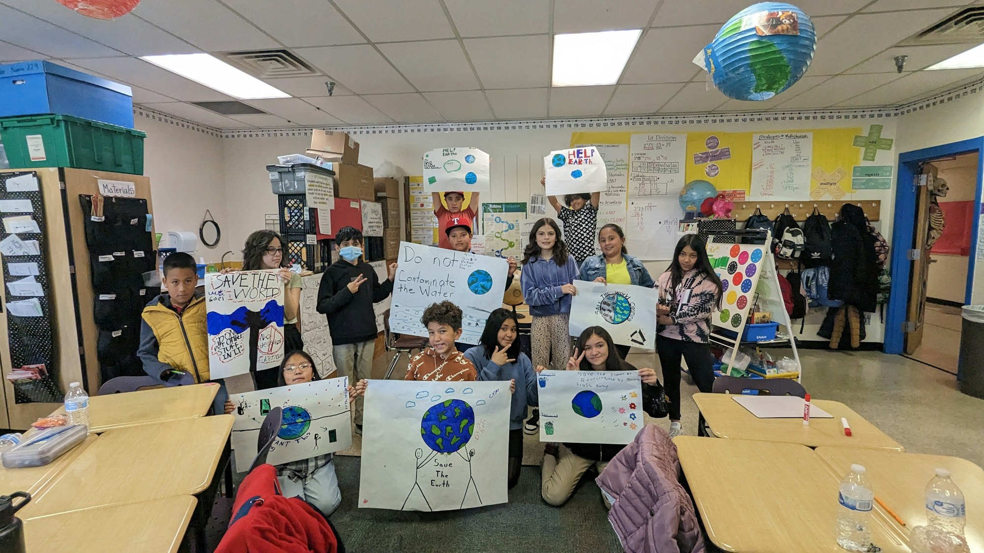 Students holding environmental awareness posters in a classroom.