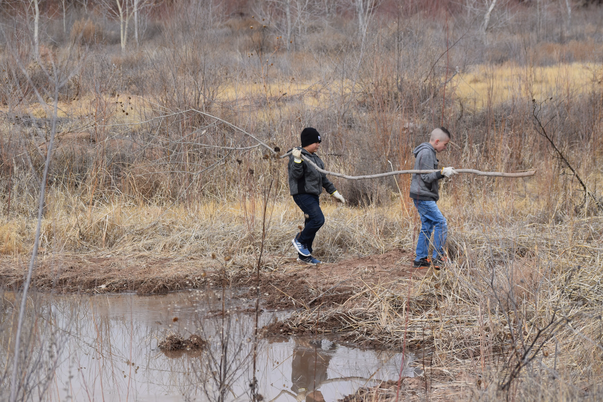 May contain: land, nature, outdoors, clothing, glove, water, person, pond, swamp, pants, footwear, shoe, plant, vegetation, hat, and wilderness