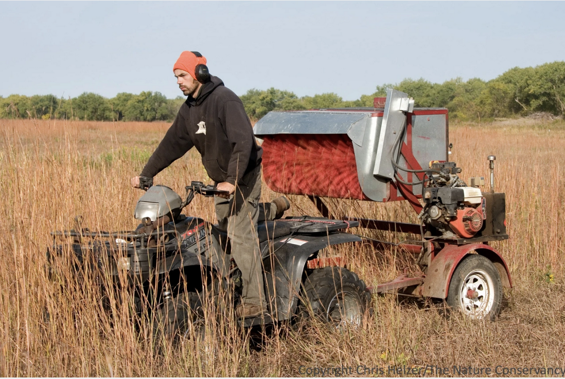 Man operating machinery in a field with dry grass.