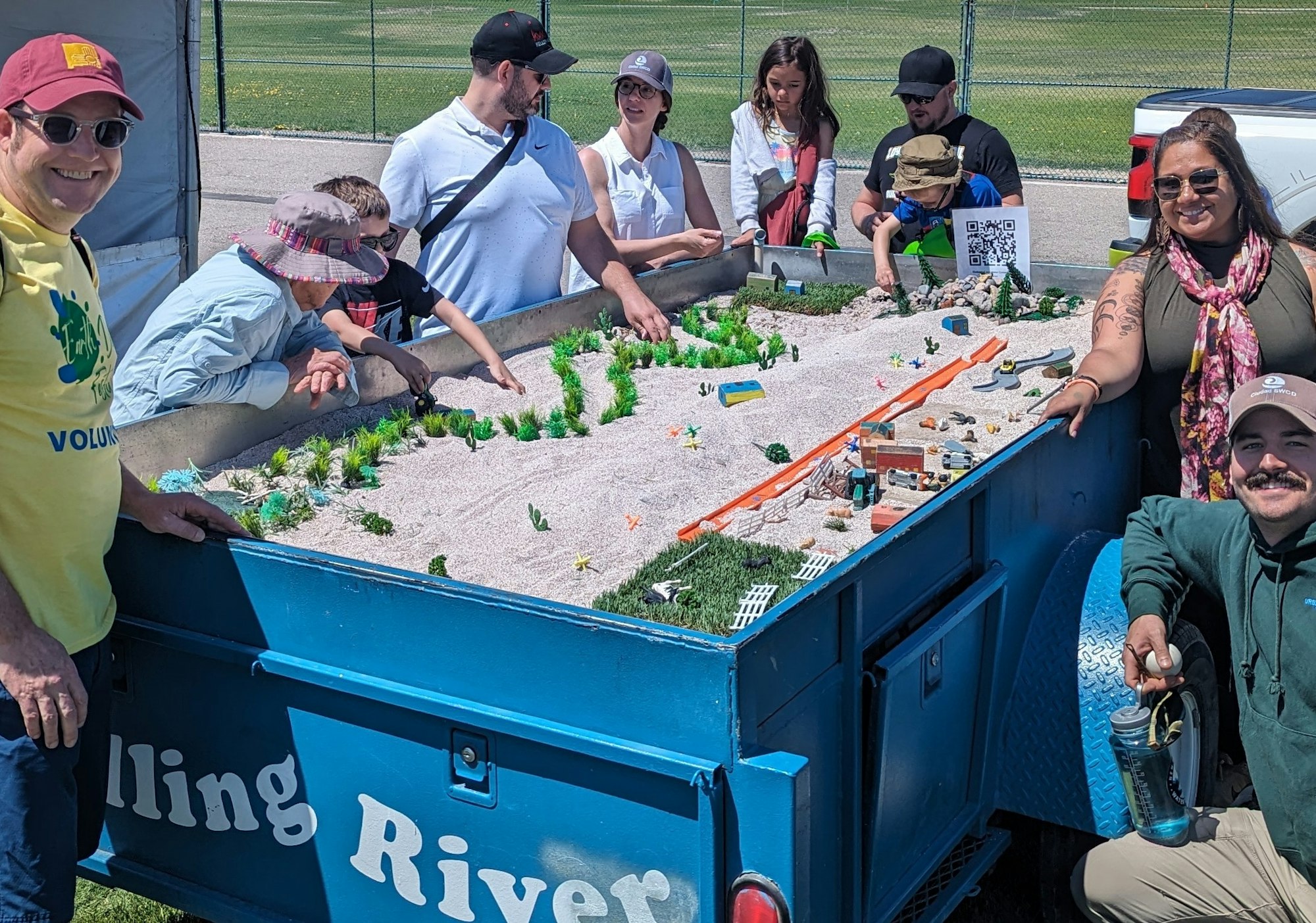 A group of people observing a mobile educational river model with interactive displays.