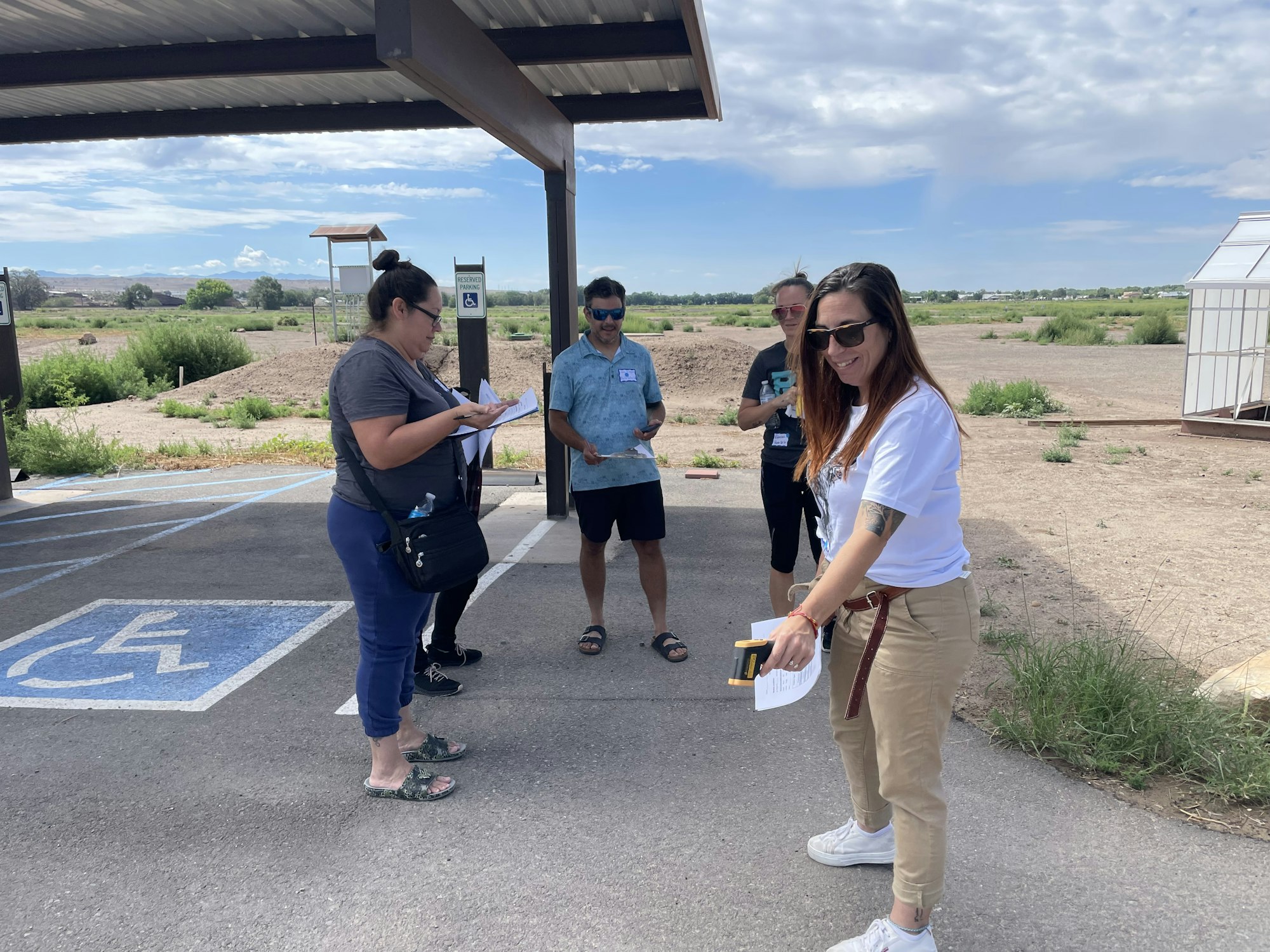 Group of people with papers, standing in a parking lot, interacting, partially sunny day.