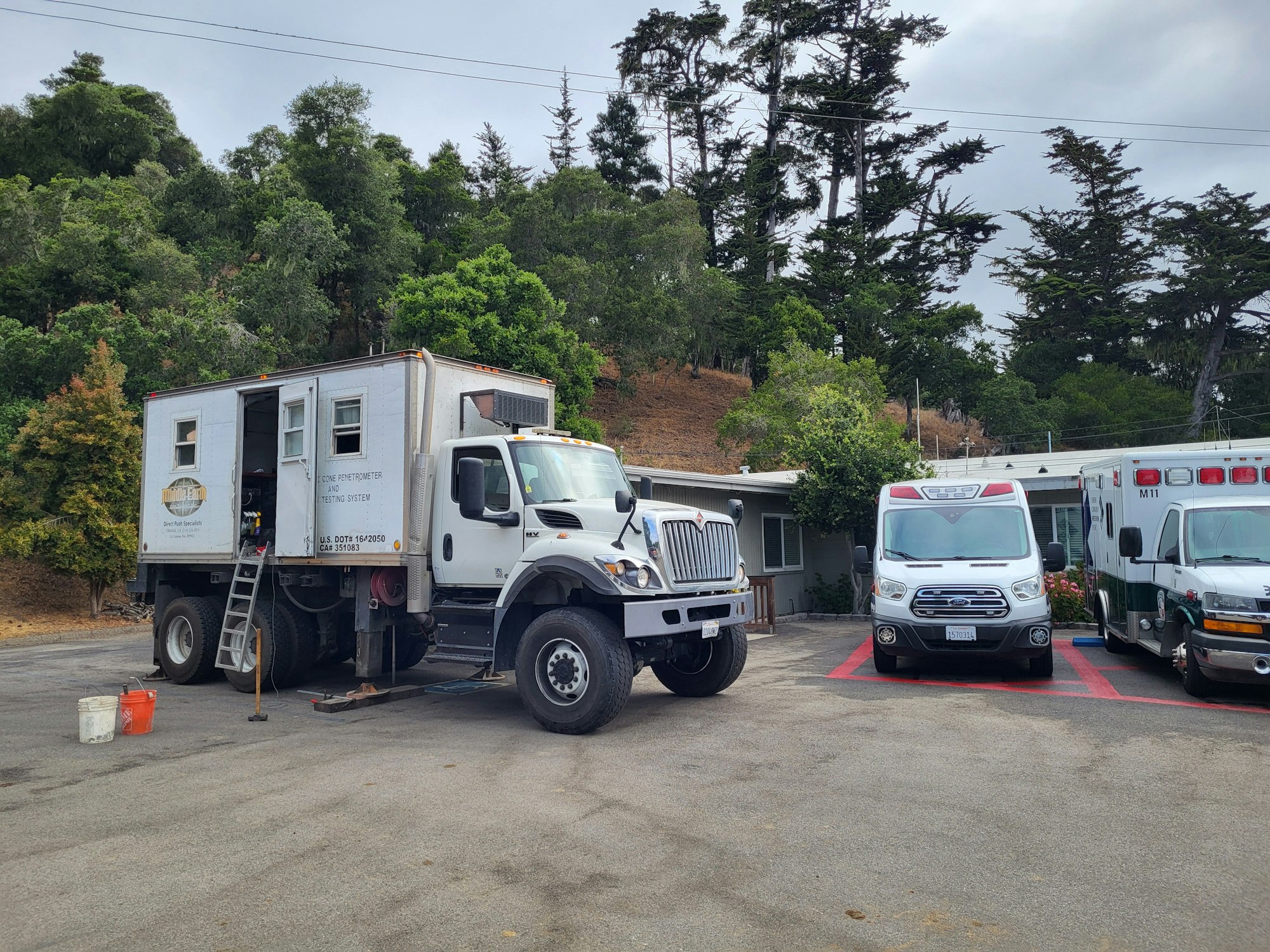 Three utility vehicles parked in a lot with trees and a building in the background.
