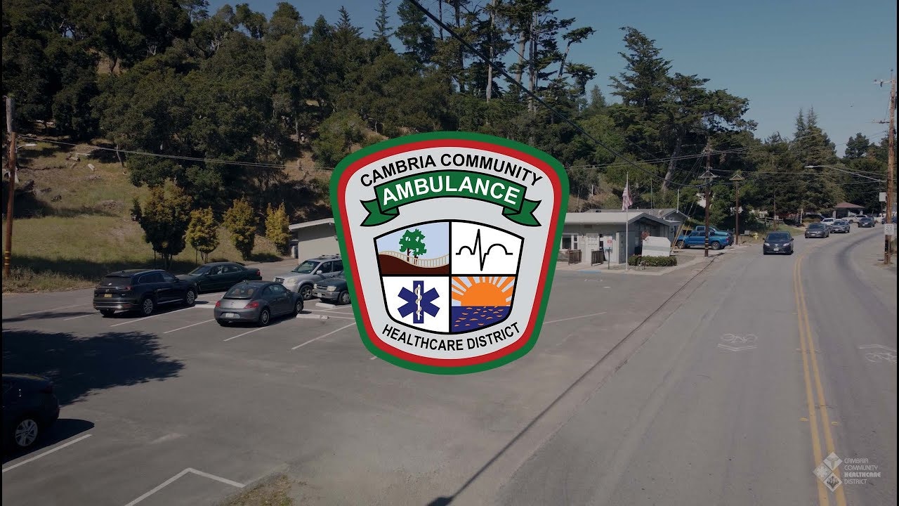 A street scene with cars and trees, overlaid with the Cambria Community Ambulance Service logo.