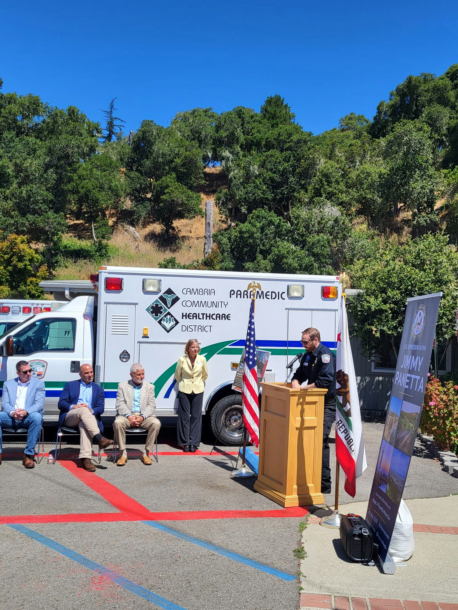 Ambulance, people gathered for an event, podium with American flag.