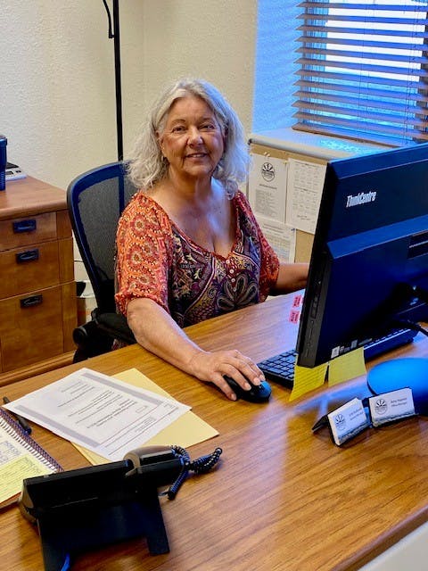 A person sitting at a desk with a computer, paperwork, and a telephone.