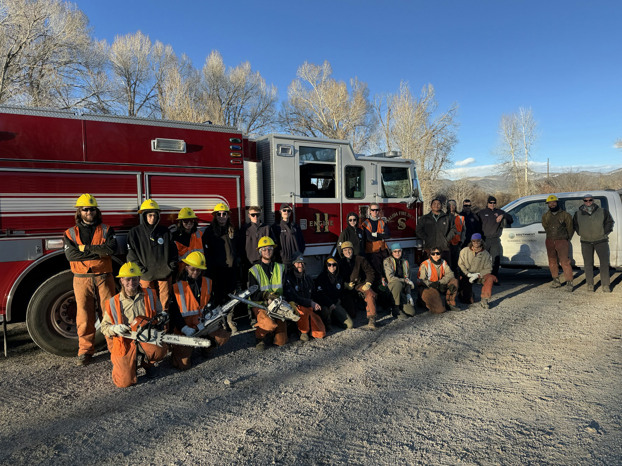 A group of people in uniforms and helmets standing together in front of a fire truck.