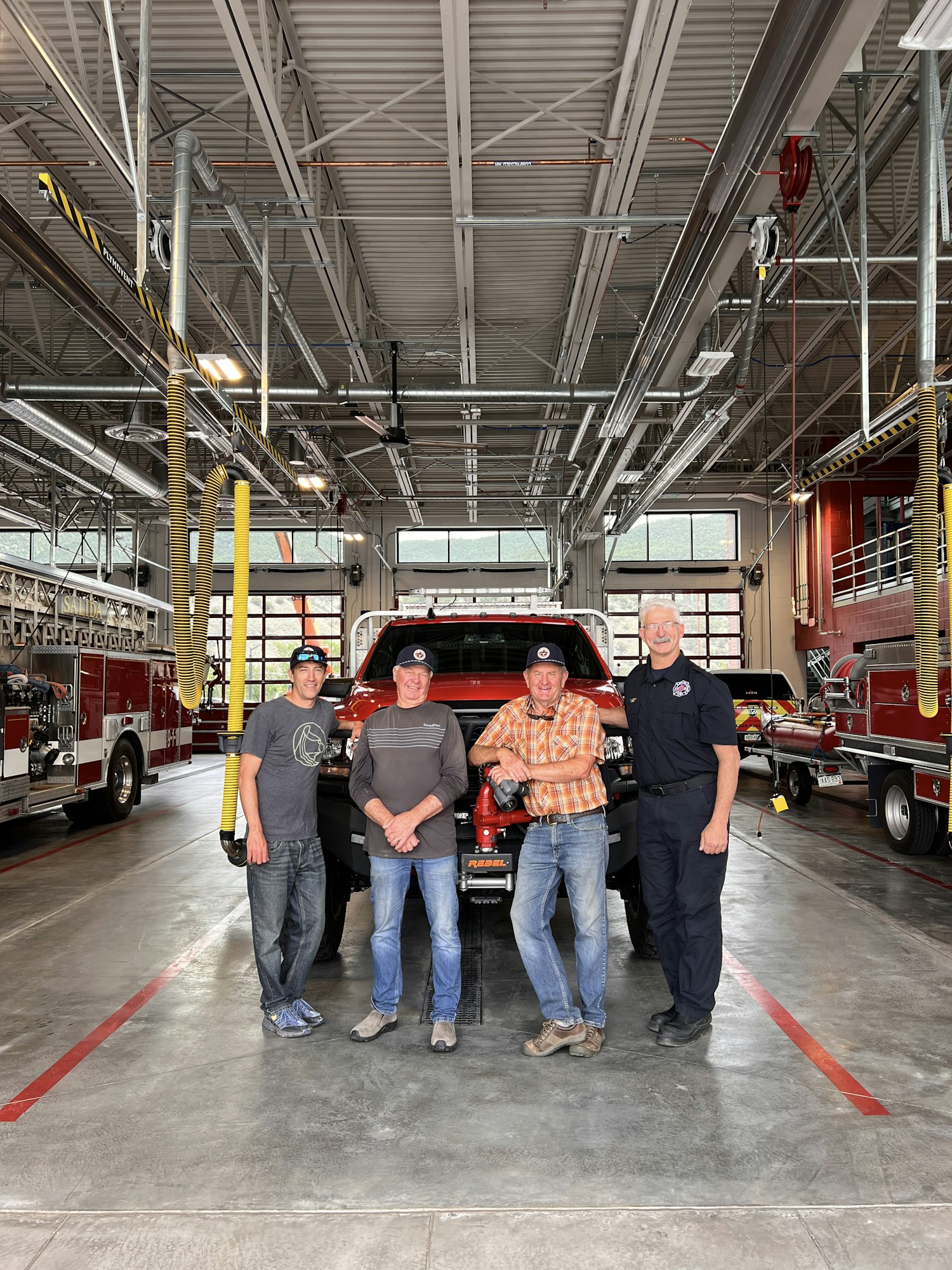 Four people standing in a fire station garage with a fire truck in the background.