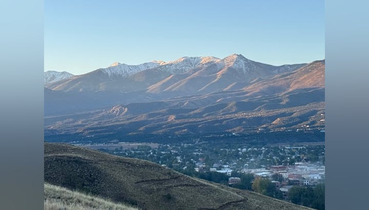 Mountain range with snow-capped peaks, overlooking a valley with buildings, during daytime.