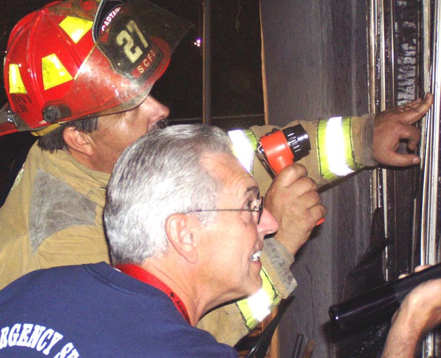 Two men in emergency response gear inspecting or working on a door.