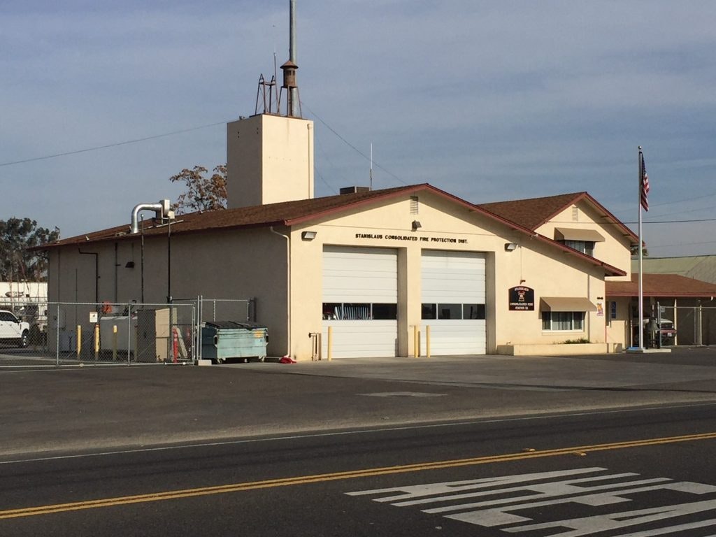 A fire station building with a garage door, an American flag, and clear skies.