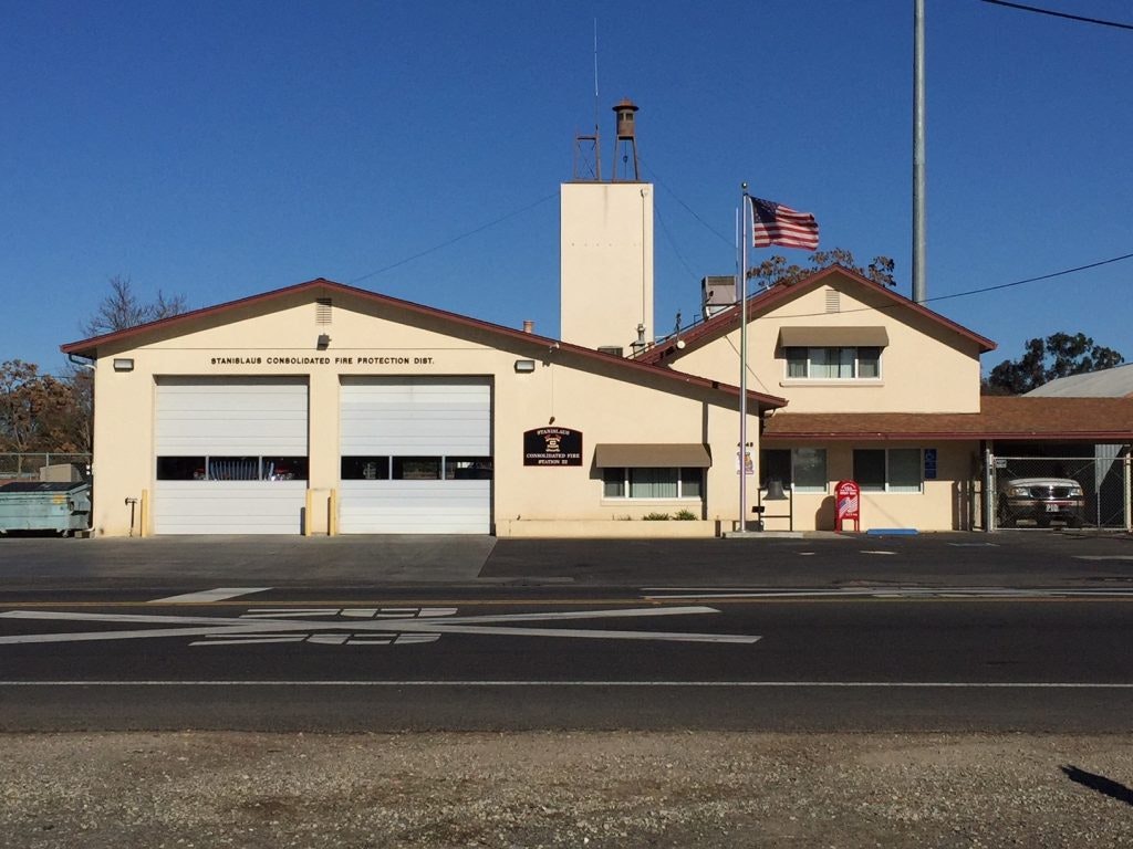 A fire station with two garages, a flagpole with the American flag, and sunny skies.