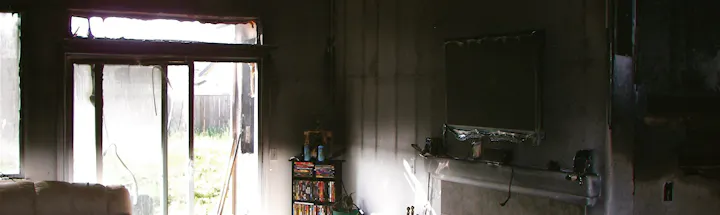 Interior of a room with fire damage, burnt window frames, damaged wall, and a blackened television set.