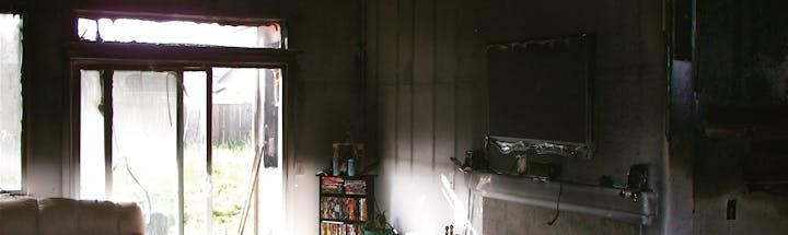 Interior of a room with fire damage, burnt window frames, damaged wall, and a blackened television set.