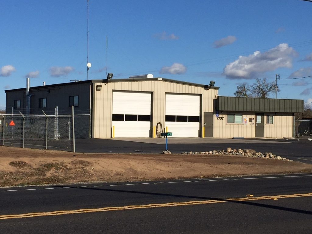A building with large garage doors, possibly a workshop or fire station, under a blue sky.