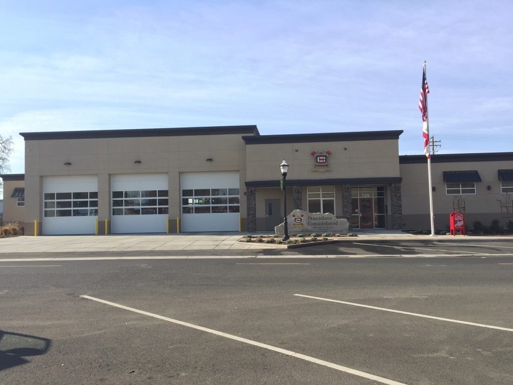 Modern fire station with two bays, American flag, clear blue sky.