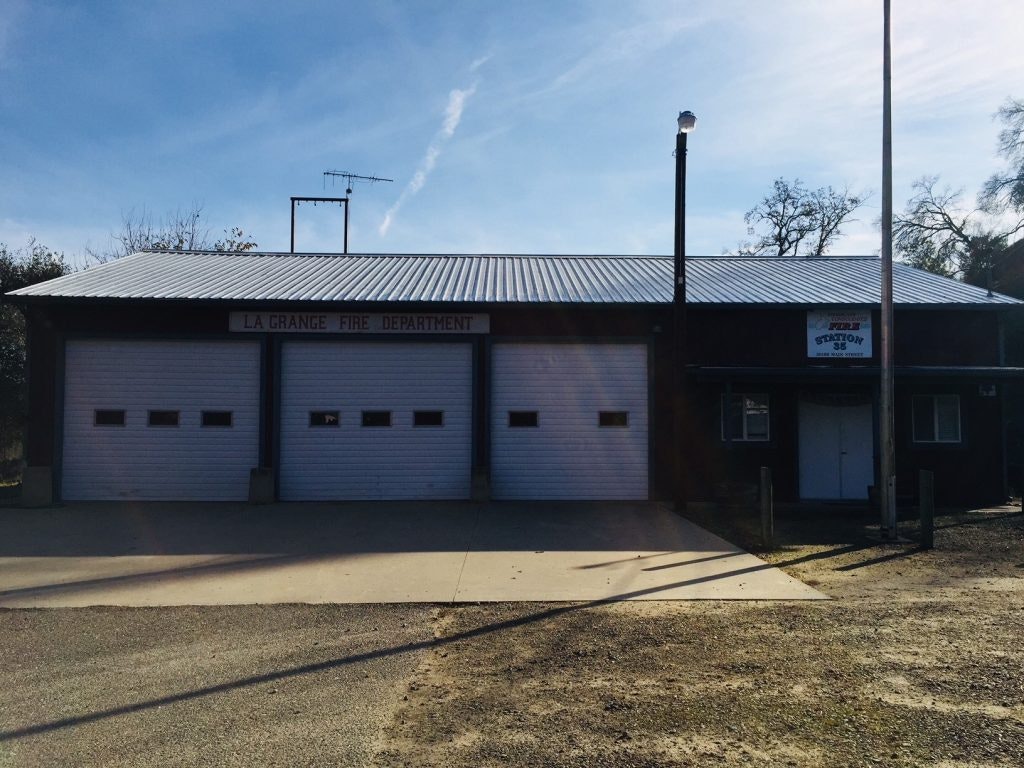 A fire department building with three garage doors labeled "LA GRANGE FIRE DEPARTMENT" under a clear sky.