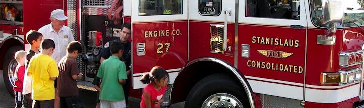 Firefighters interacting with children near a fire engine.