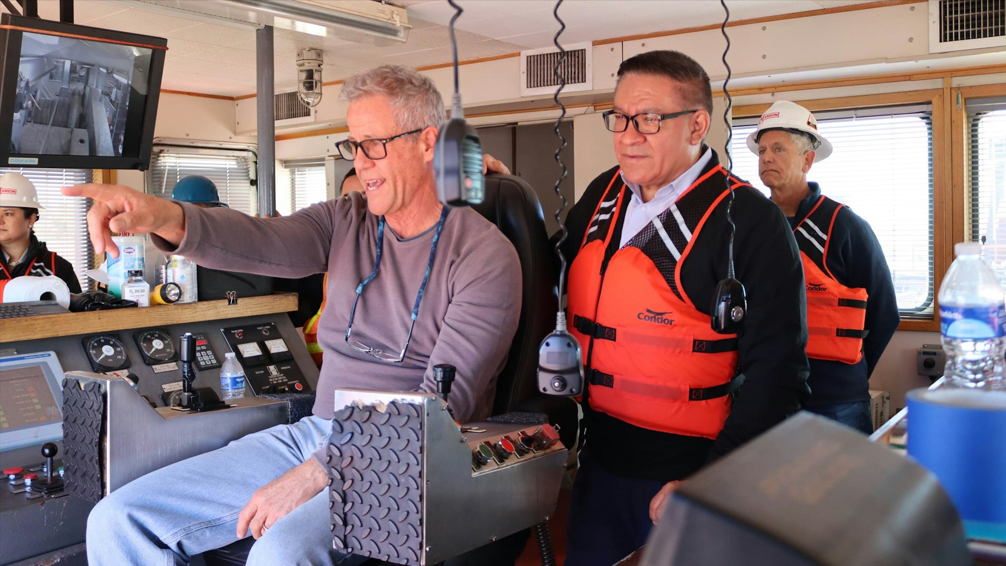 People with safety gear inside a control room, possibly for training or operations, with monitors and control panels.