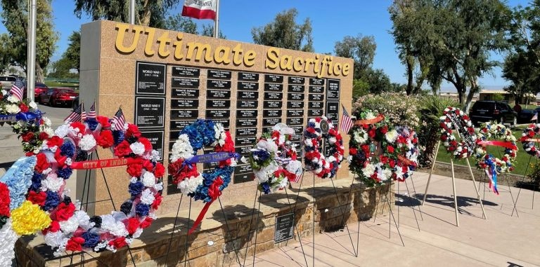 A memorial wall titled "Ultimate Sacrifice" with wreaths decorated with flags in front.