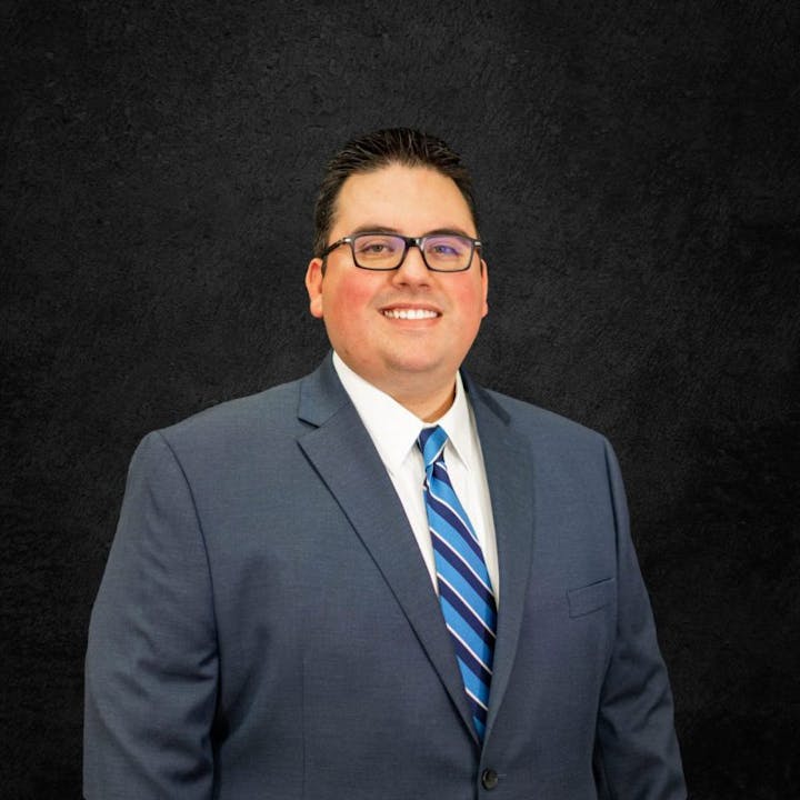 A person in a suit and tie, smiling against a dark textured background.
