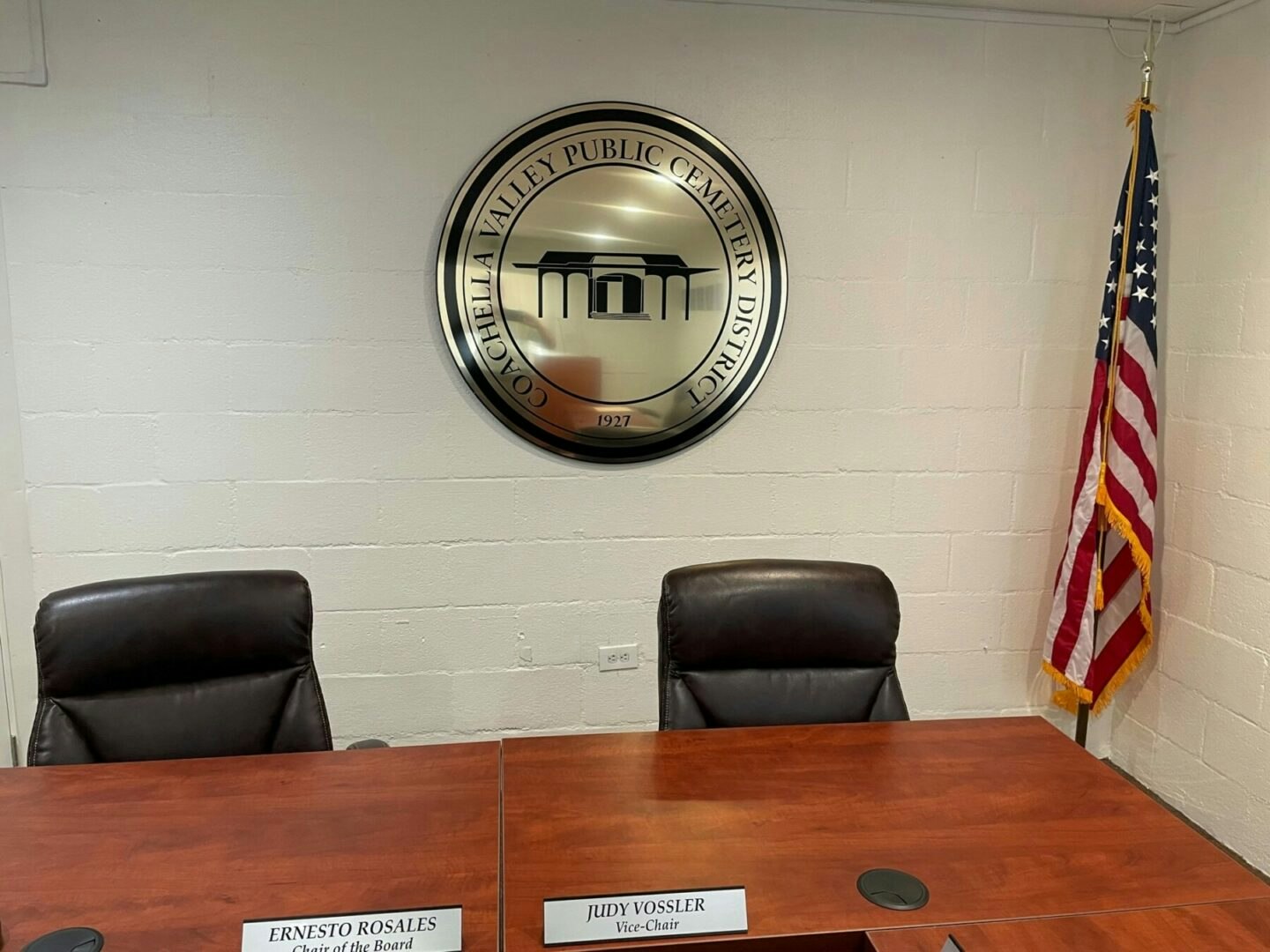 Meeting room with two chairs, nameplates, Coachella Valley Public Cemetery District logo, and U.S. flag.
