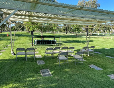 Outdoor setup with a covered canopy, folding chairs, and green grass in a park-like setting.