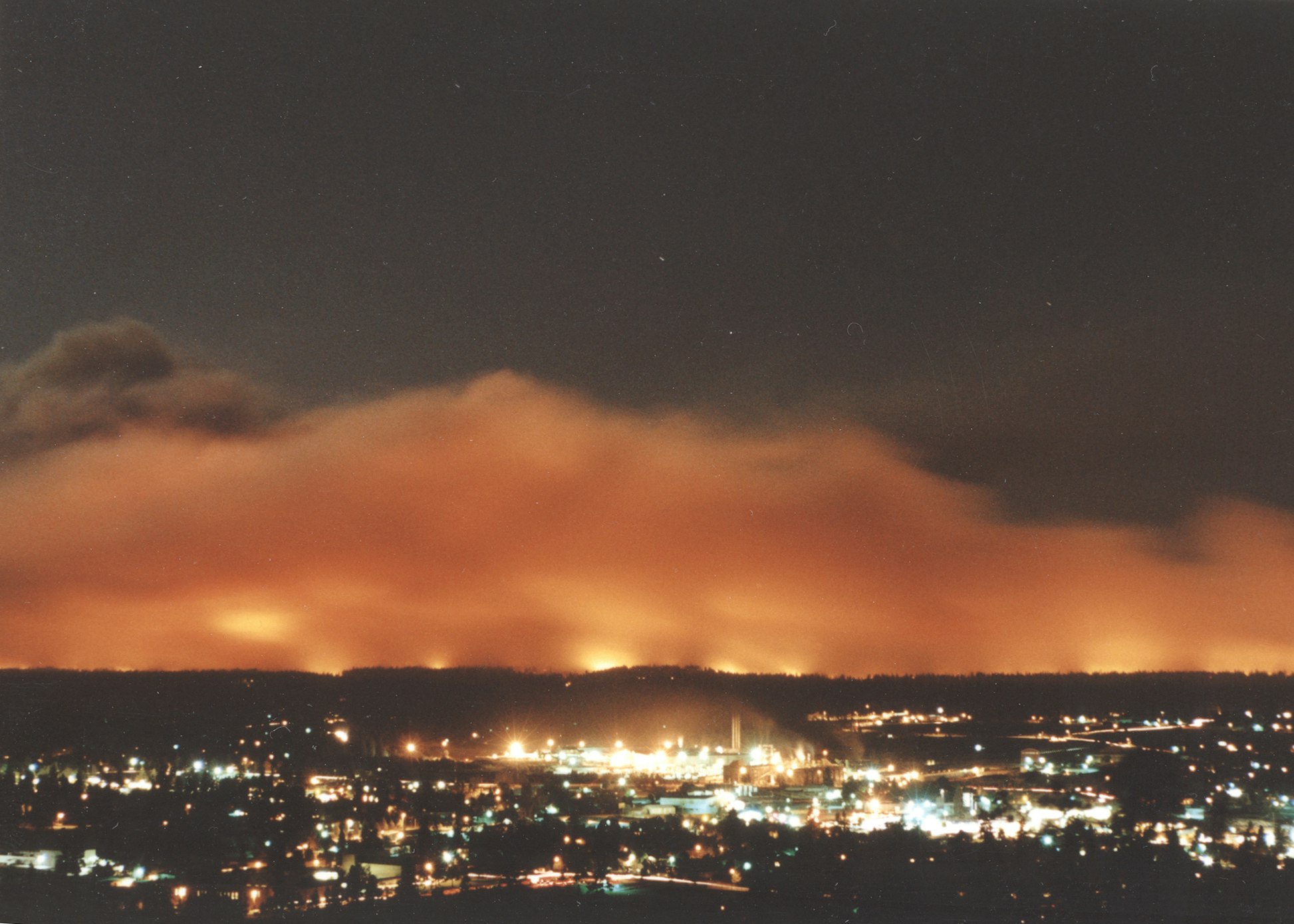 A cityscape at night with a glowing orange sky, possibly from a fire in the distance.