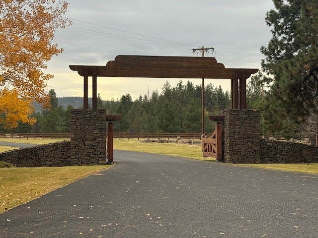 A stone and wood entrance gate on a paved driveway, surrounded by trees and autumn foliage.