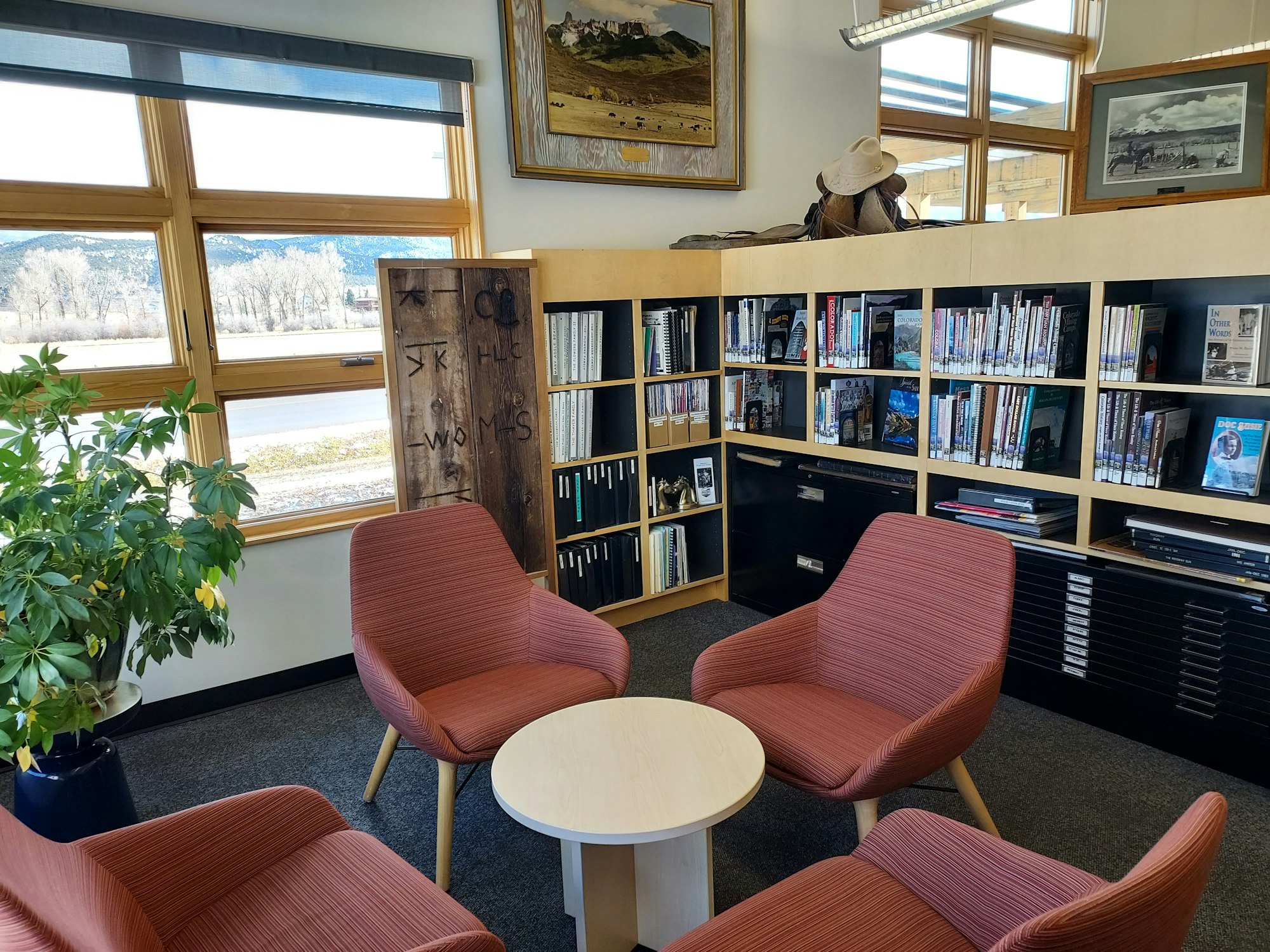 May contain: chair, furniture, clothing, hat, book, indoors, library, publication, plant, lamp, art, painting, person, architecture, building, and lounge