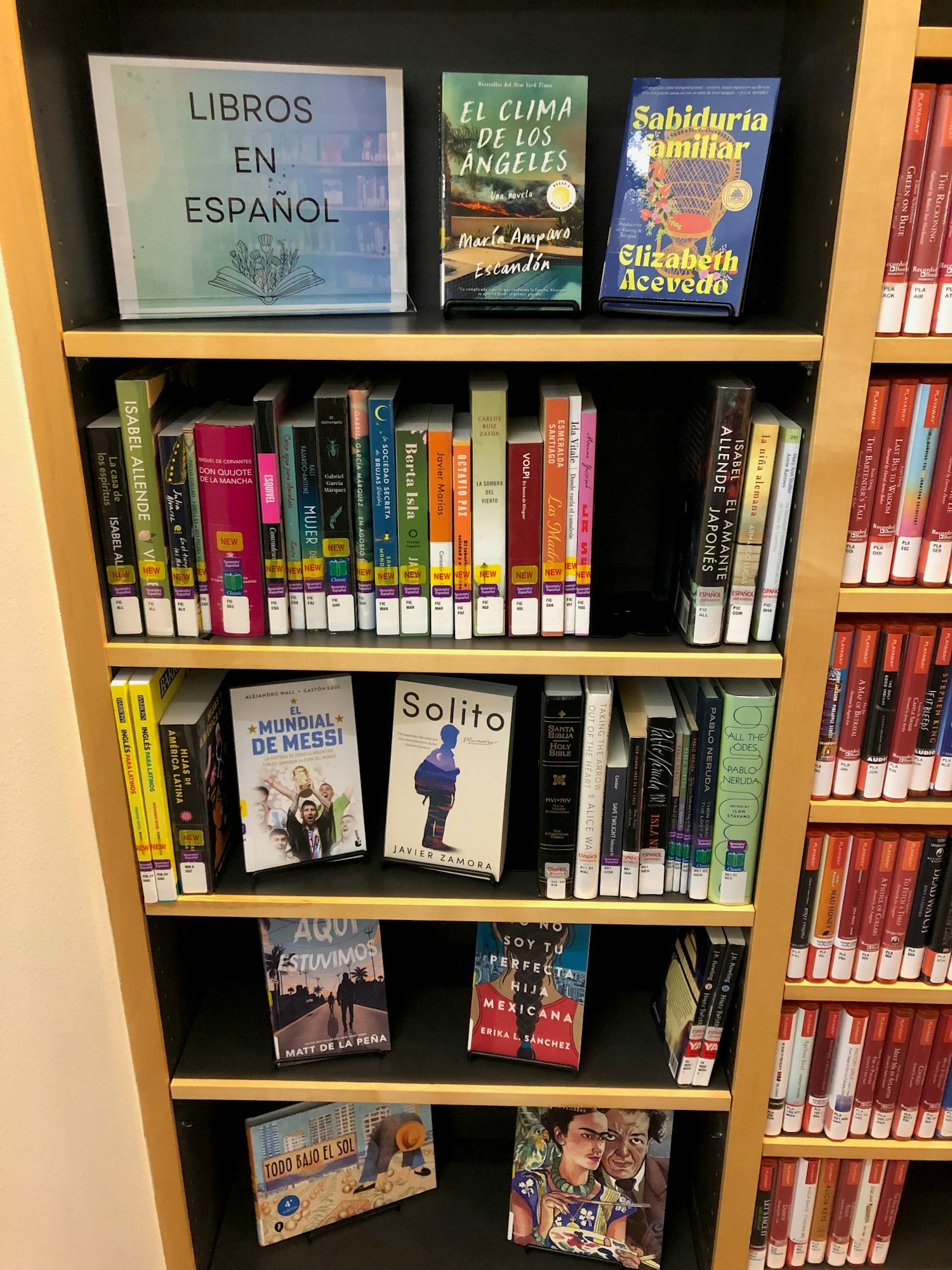 A bookshelf with a mix of Spanish books, some horizontally stacked and a sign saying "LIBROS EN ESPAÑOL."