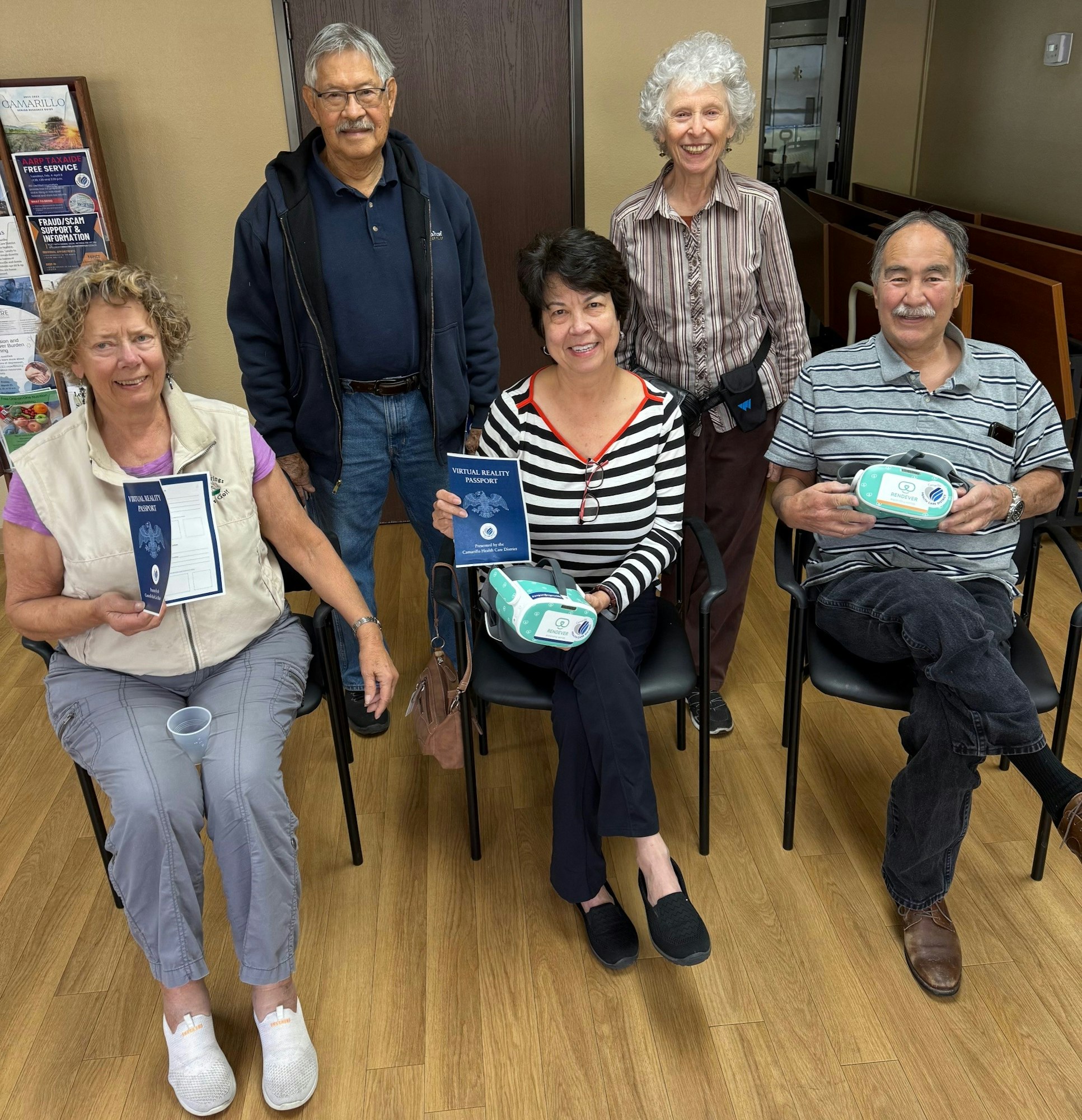 A group of five people holding virtual reality passports and VR headsets, seated in a room.