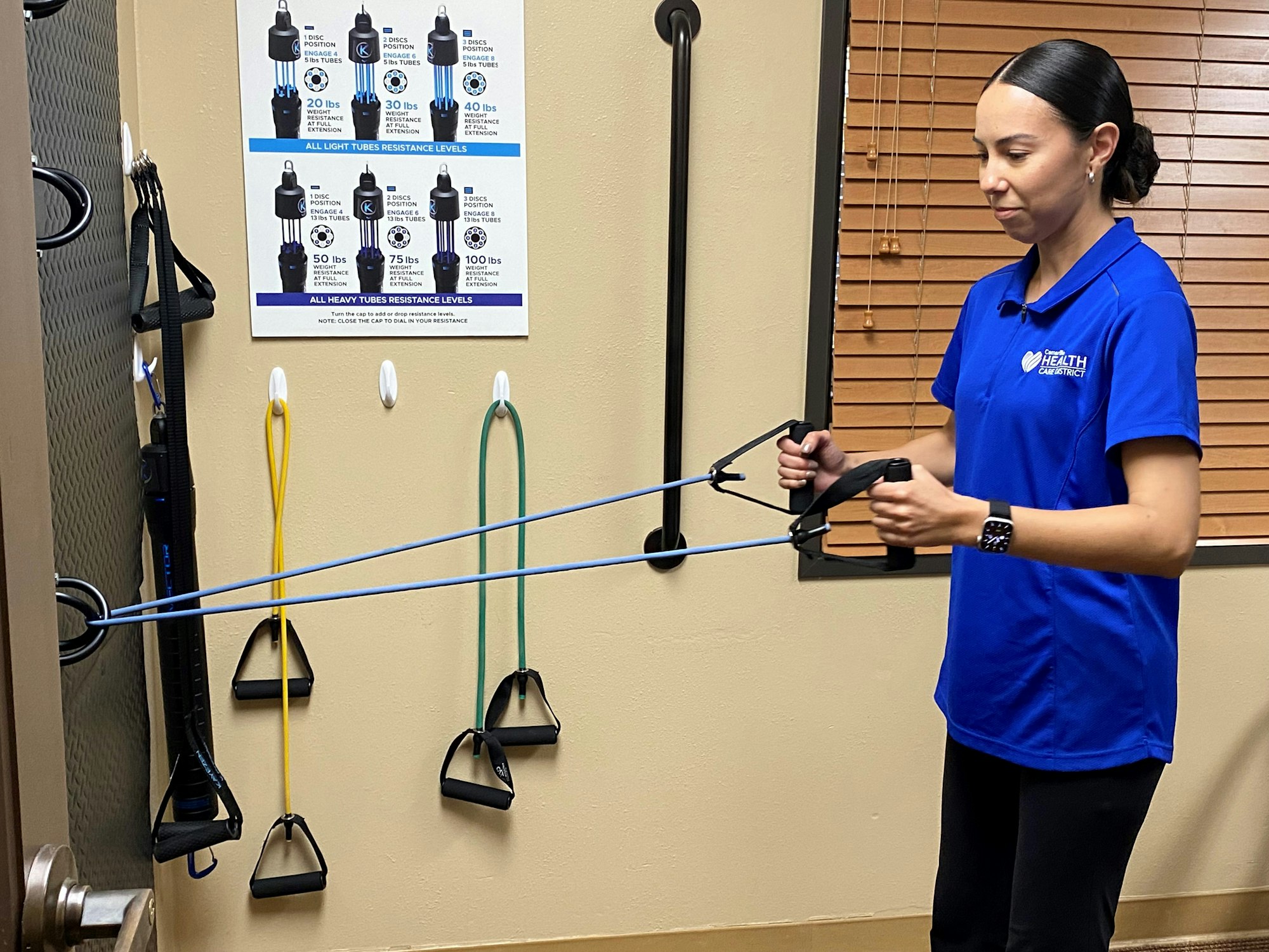 A person exercising with resistance bands in a gym, with a resistance level chart on the wall.