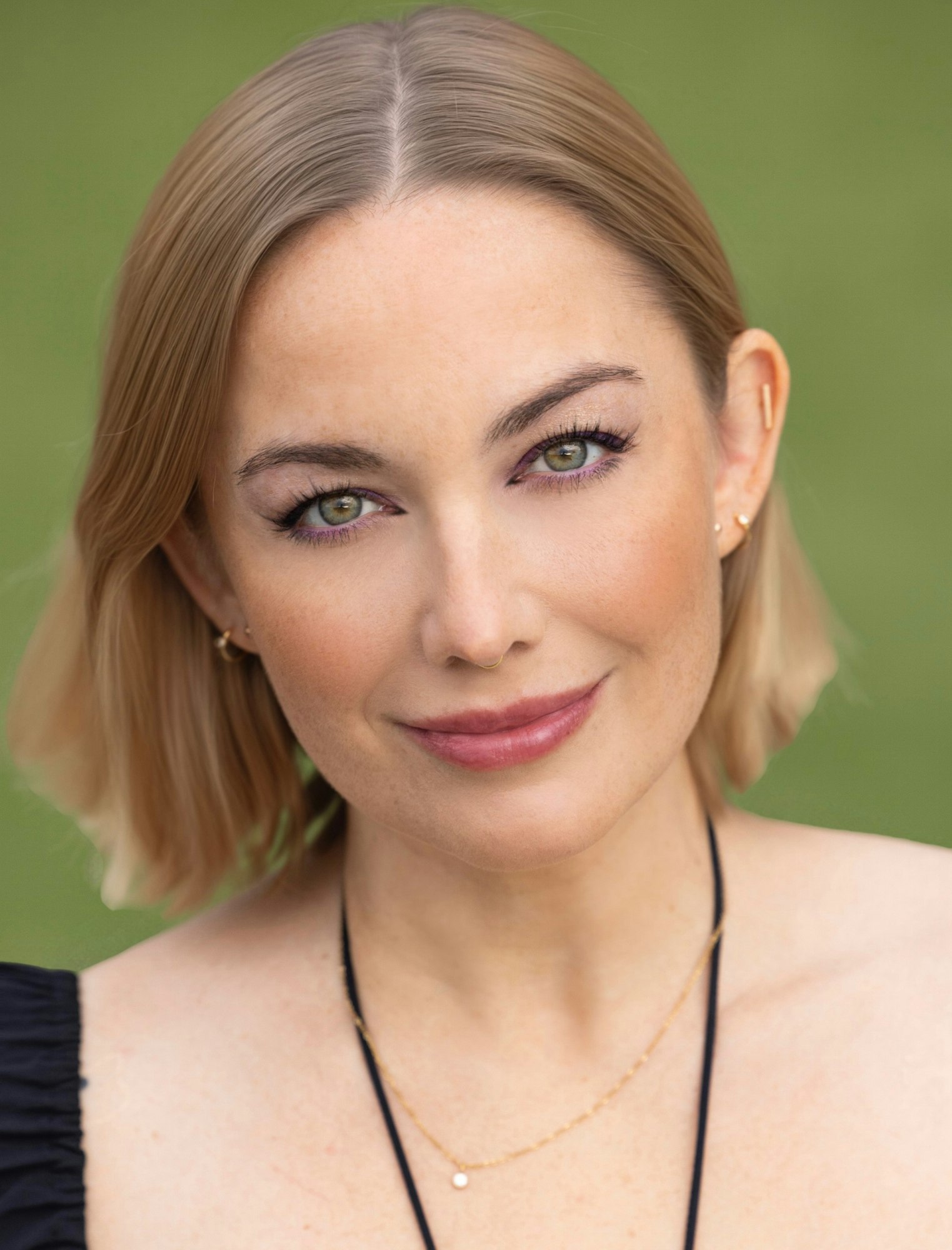 A woman with short blonde hair and subtle makeup smiling against a green background.