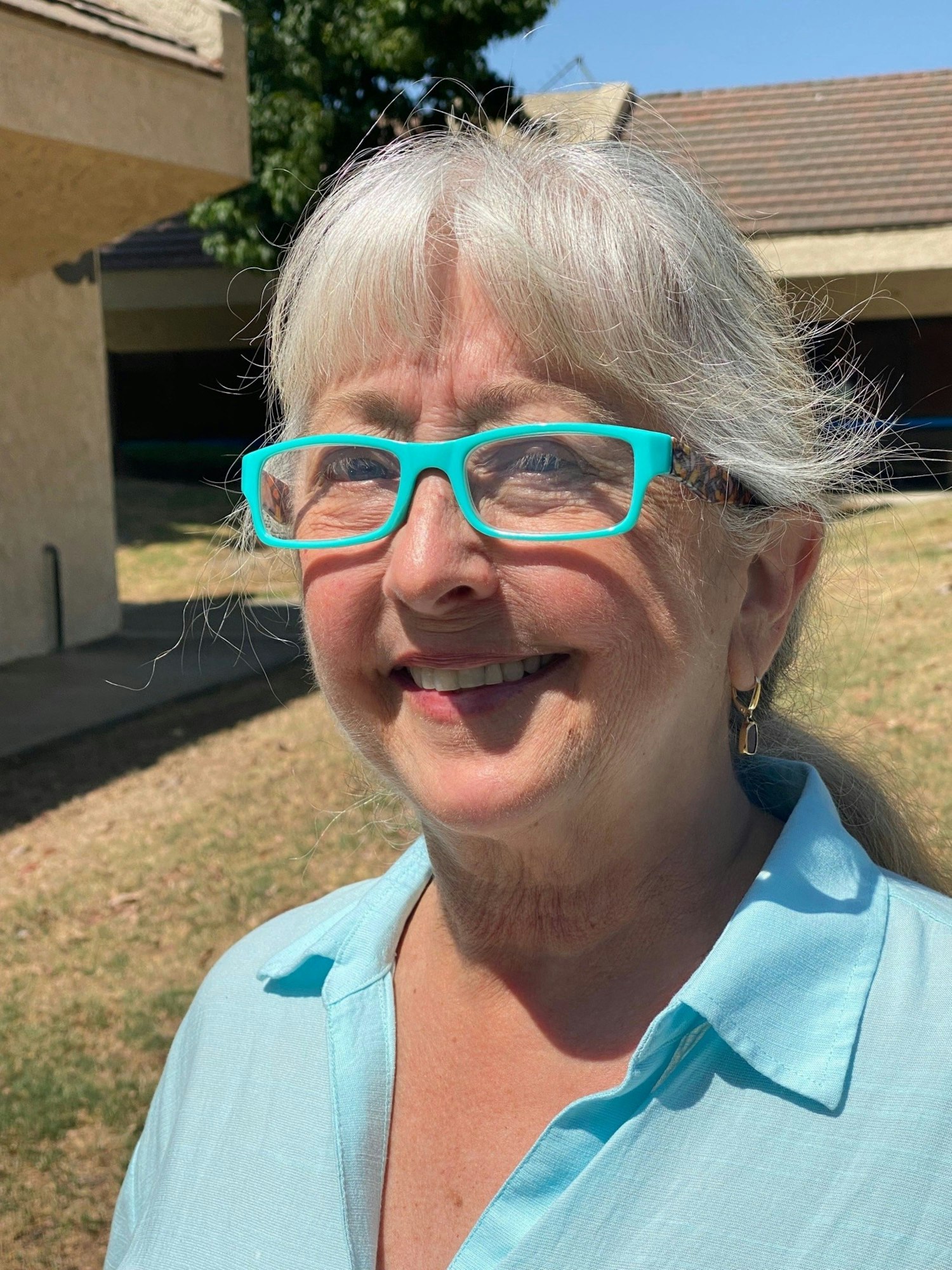 Smiling person with turquoise glasses and shirt, outdoors.