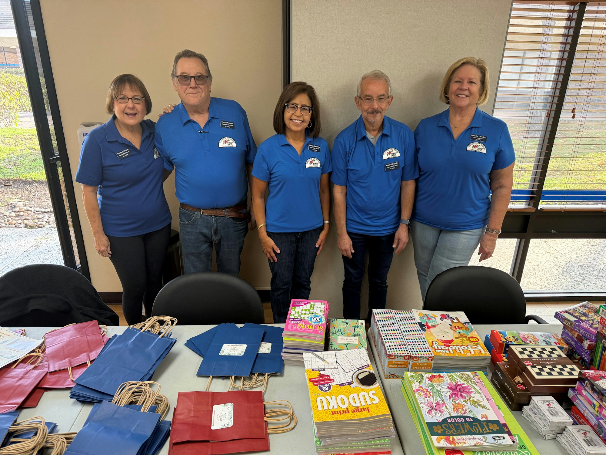 Five people in blue shirts stand behind a table with colorful books and gift bags.