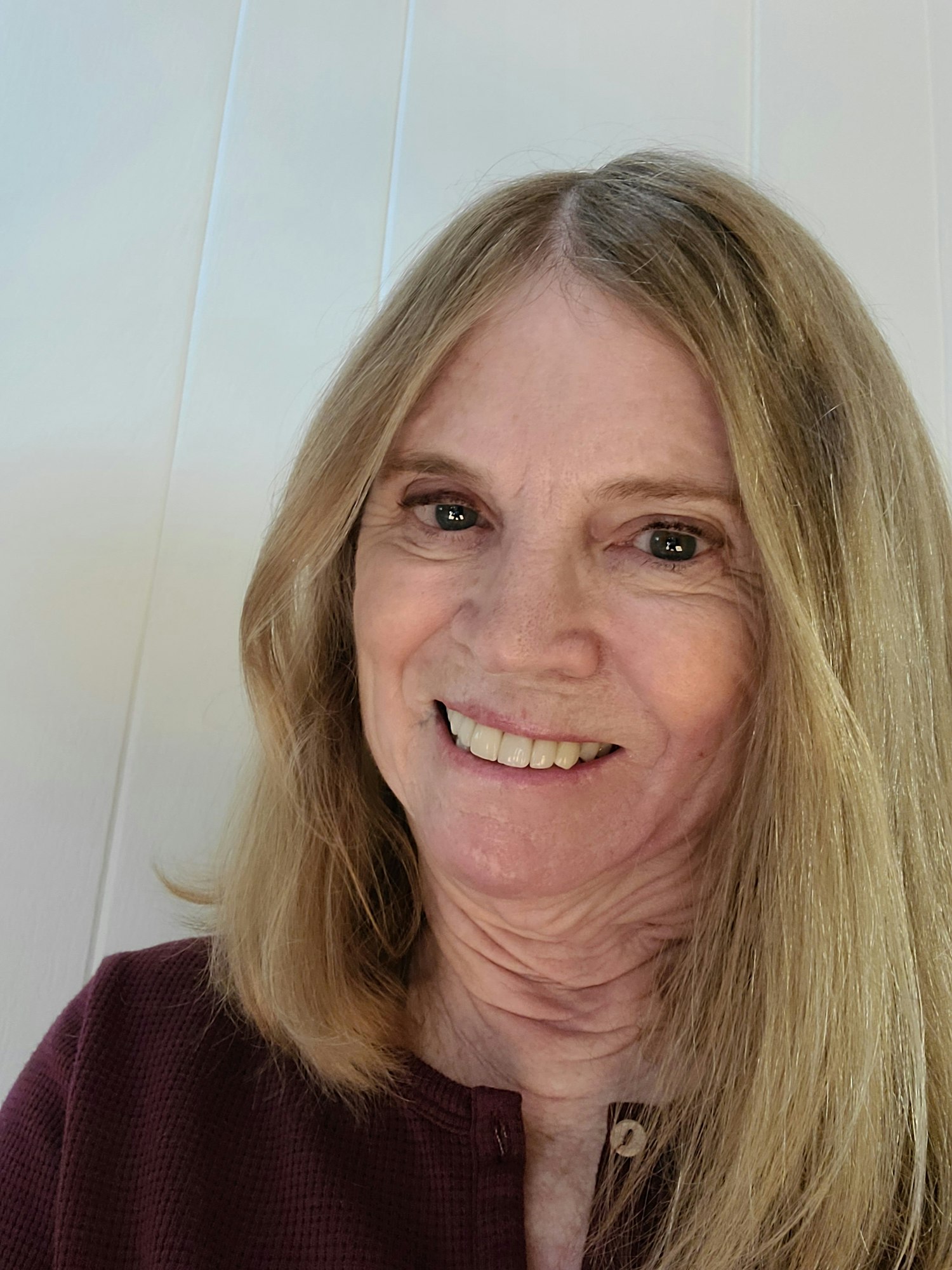 A smiling woman with long blond hair, wearing a burgundy shirt, against a white background. (Note: Image is rotated 90 degrees)