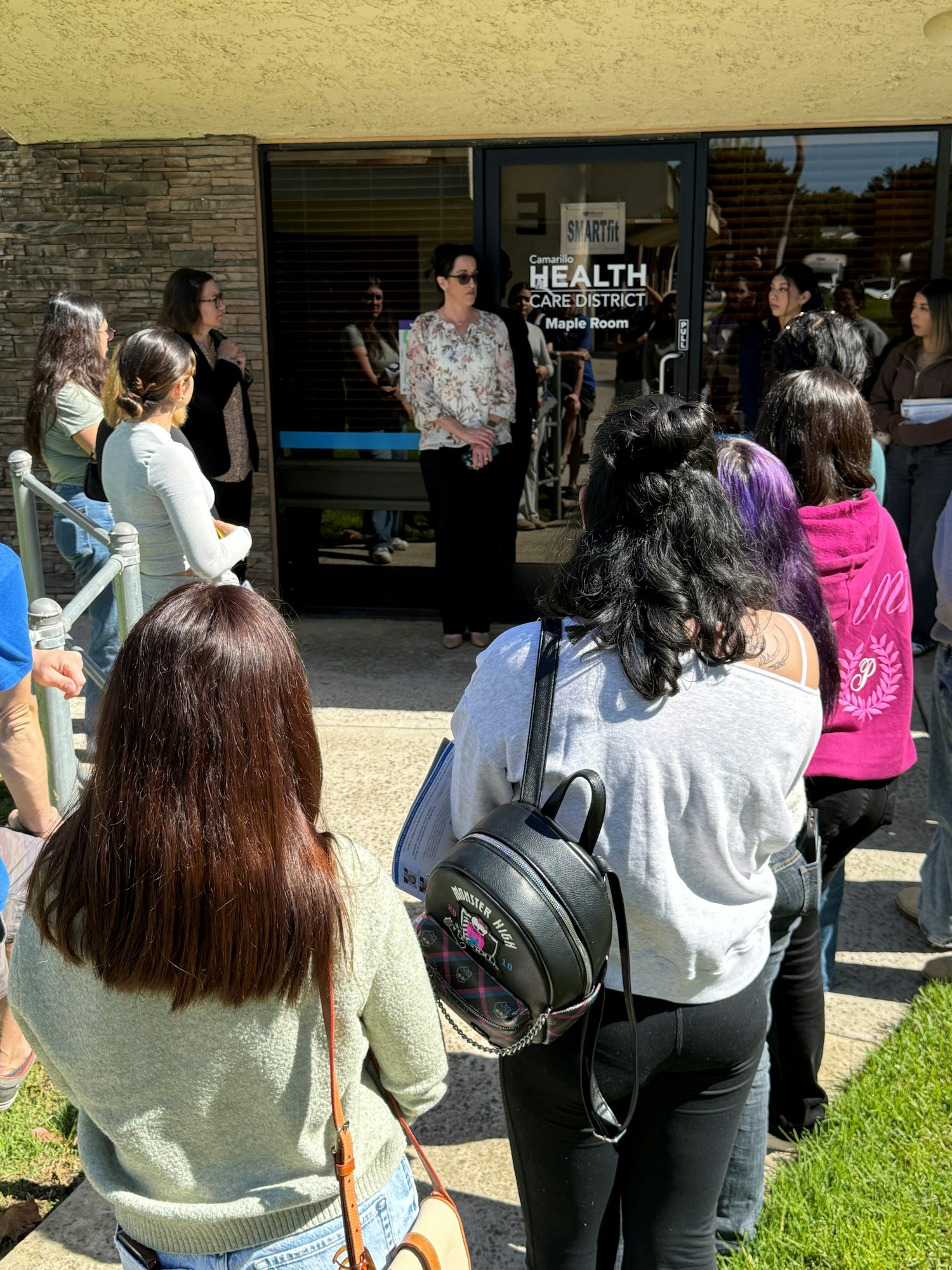 A group of people gathered outside a building with a sign reading "Camarillo Health Care District Maple Room."