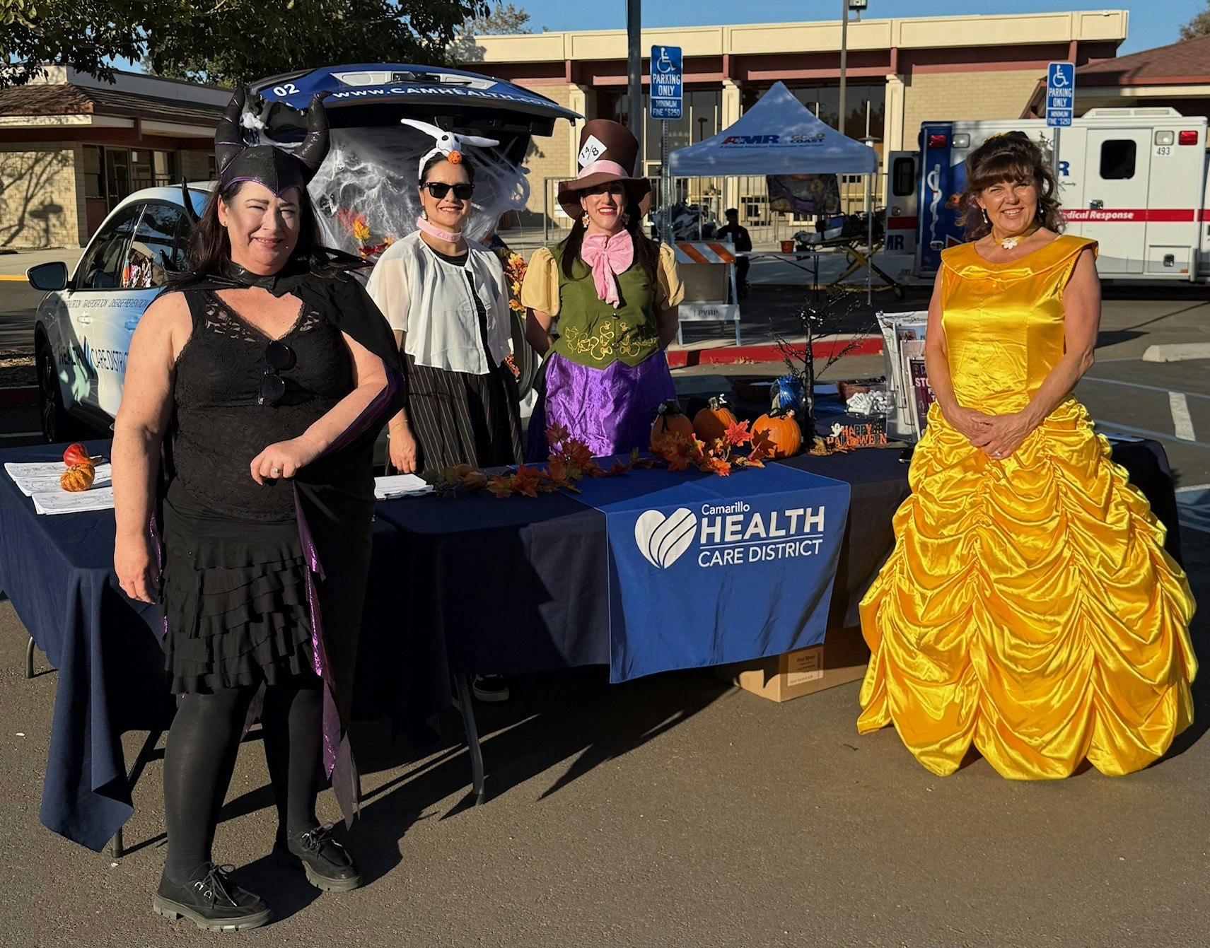 Four people in costumes at a Camarillo Health Care District booth with autumn decorations.