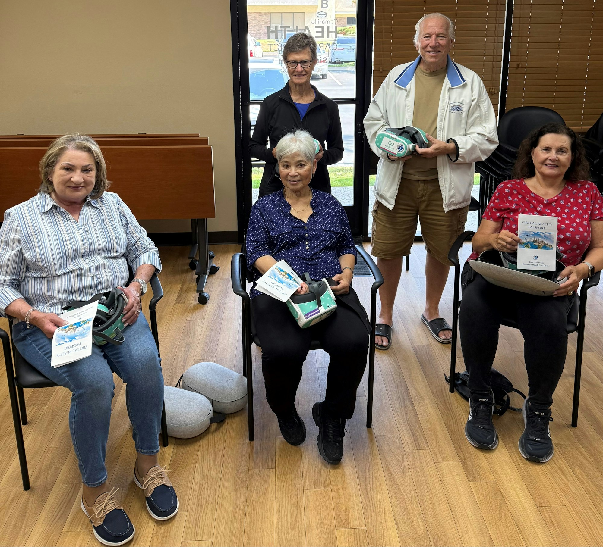 Six people in a room, some seated, holding VR headsets and booklets.