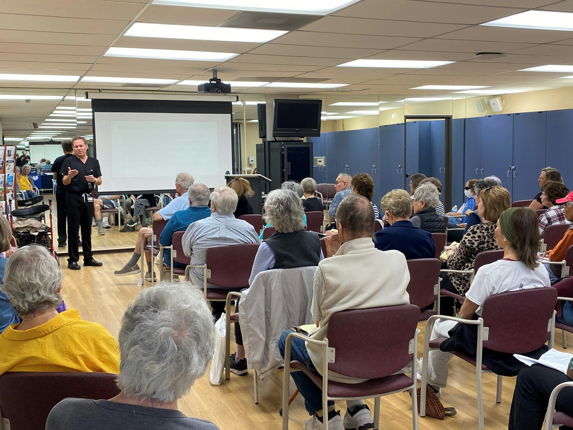 A presentation with an audience and a speaker in front of a projection screen.